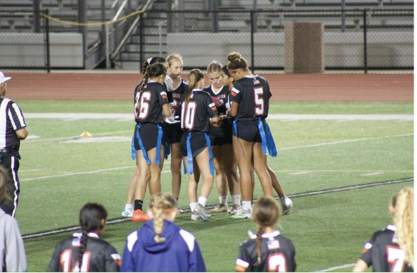 Varsity girls flag football team huddling up to figure out a play to use during the game. 
