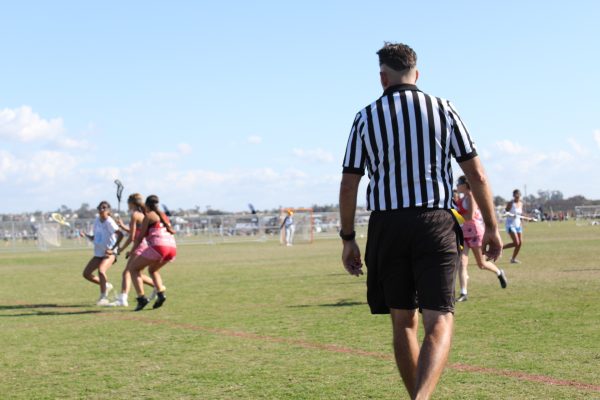 The referee closely observes girls lacrosse game at a tournament. 