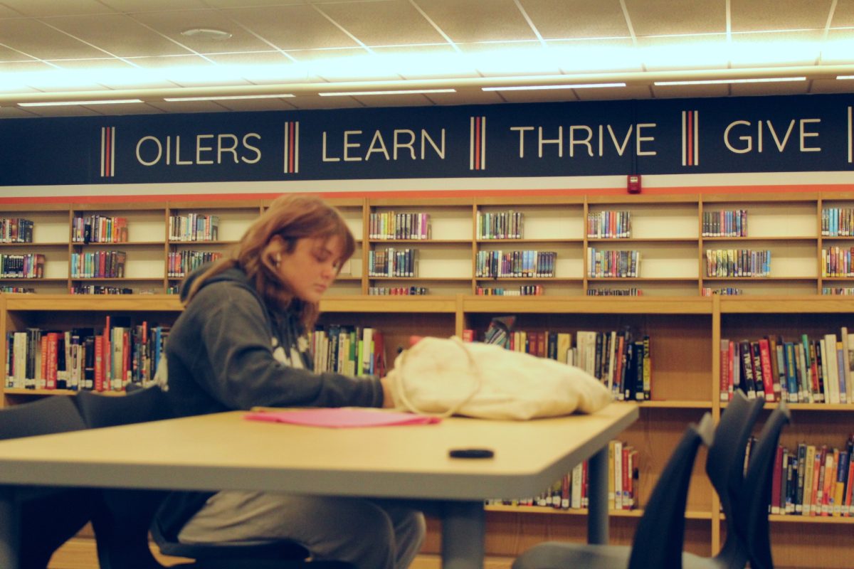 An HBHS student sits at a library table studying and doing homework.