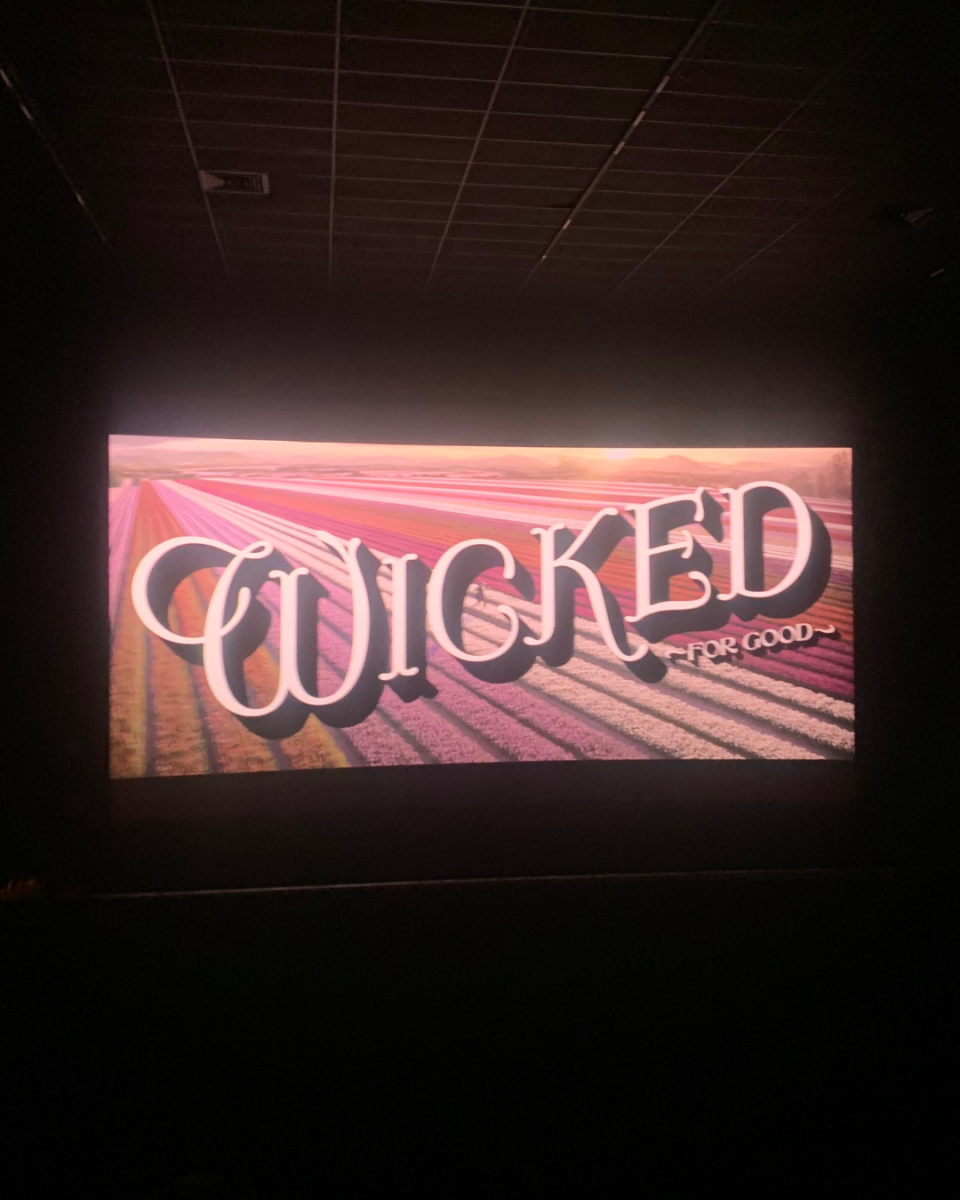 The beautiful title card of "Wicked: For Good" lights up a crowded theater.