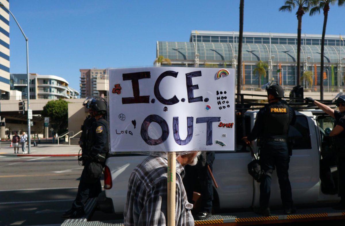A protestor holds an "ICE out" sign during march while walking past police.